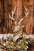 Silberfarbener Hirschkopf in einem Kranz vor Vintage Holzwand