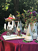 Dekorative Papierhütchen, Kerzenhalter und Blumenstrauß auf Gartentisch