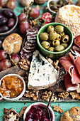 Cheese and meat board with cheese, Serrano ham, fuet, bread, olives, tomatoes, grapes, nuts, and jam