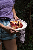 Frau serviert ein Stück Hefekuchen mit Aprikose und Himbeeren im Garten