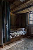 Single bed with a privacy curtain in room with repurposed wooden ceiling