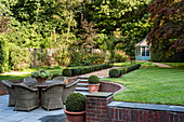 Rattanmöbel auf Terrasse, gepflegter Garten mit Buchsbaumhecke und Gartenhaus