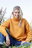 Junge blonde Frau in gelbem Rollkragenpullover und Jeans in der Natur