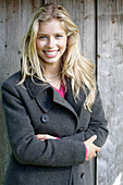 Young blond woman in a gray wool coat in front of a wooden wall