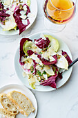 Salad with radicchio, chicory and parmesan served with a glass of orange wine on white background
