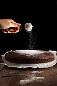 Icing sugar sprinkled by hand on to a chocolate cake