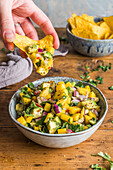 Bowl of mango salsa with some being scooped out on a tortilla crisp