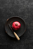 Granatapfel mit Messer in schwarzer Keramikschale