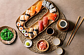 Sushi rolls set. Traditional japanese dish sushi and rolls with fresh salmon, tuna, eel and prawns on rice. Serving on wooden plate with soy sauce, sake and wakame salad on brown background. Flat lay.