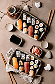 Sushi rolls set for two. Traditional japanese dish sushi and rolls with fresh salmon, tuna, eel and prawns on rice. Serving on plates with soy sauce and sake on brown table. Flat lay