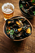 Close up of a bowl of mussel marinieres with parsley, and beer on wooden table