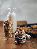 Homemade granola in glass jar near cooking tray on wooden kitchen table