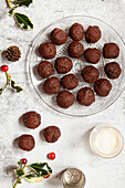 Chocolate truffles on a glass plate with holly and a pine cone alongside