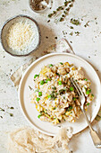 A plate of chicken, leek and pea risotto with a bowl of parmesan cheese alongside it