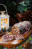 A part sliced chocolate salami on a wooden board.