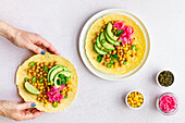 Hand touching tasty taco with ripe avocado slices and chickpea filling served on table