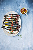Sardinen garniert mit würziger Ölsauce auf ovaler Platte und blauem Tisch