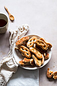 Bunch of fresh tasty pretzels served in bowl near napkins and cup of coffee on gray table during breakfast
