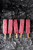 Yummy fruit ice pops placed in row on heap of ice cubes in fridge