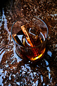Glass of whiskey with cinnamon on wet table