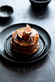 Stack of yummy pancakes with maple syrup and fig slices served for breakfast on plate on gray table
