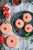 Tasty cakes with jelly balls and pink icing served on round tray near red carnations