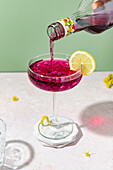 Brombeerlikör aus der Flasche in elegantes Glas mit Zitronenscheibe giesssen
