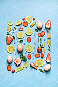 Composition of thin slices of fresh sour lemon lime and strawberry with greens and eggs on blue geometric background