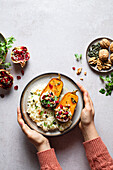 Crop anonymous female with plate of delicious halved roasted pumpkin served with rice greens and pomegranate seeds on gray background with walnut