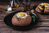 Tasty round loaf of bread with fried egg served on black plate on wooden table with cutlery in light restaurant