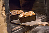 Freshly baked loaves of bread with crust placed on wooden cutting board in oven of light bakery