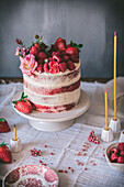 Delicious red velvet cake with fresh strawberries and flowers served on table during holiday celebration in kitchen near candles