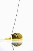 Healthy green oval olive with cut on spilled yellow oil placed on reflective surface