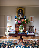 Antique table with books and bouquet of flowers in front of chest of drawers, Egyptian carpet in a drawing room