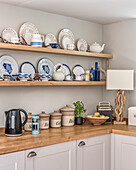 Shelves with blue and white crockery above kitchen counter, table lamp with driftwood base