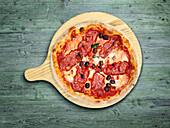 Salami pizza with olives on a wooden board