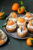 Orange and poppy seed cupcakes with cream cheese frosting and whole peeled tangerine
