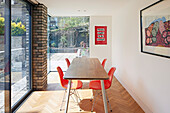 Red shell chairs in a narrow dining room with floor to ceiling windows
