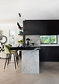 Designerküche mit schwarzen Fronten und Marmorelementen, Barhocker mit grüner Polsterung
