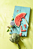 An artichoke and a slice of watermelon with the letter 'L' cut from it