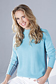 Blond woman wearing a light blue sweater and white trousers