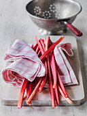 Rhubarb stalks on kitchen towel, in the background is a colander