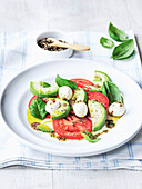 Tomaten-Avocado-Salat mit Mozzarella, Basilikum, Olivenöl und schwarzem Pfeffer