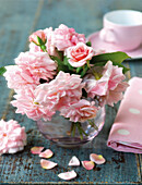 Vase mit rosa Rosen mit rosa Teetasse und Serviette