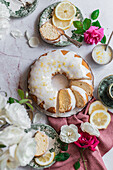 Top view of a sponge lemon cake on a table next to other plates with lemon slices and flowers with petals