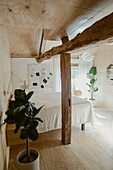 Sleeping area with queen bed, in the foreground houseplant and rustic wooden support beams