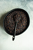 Raw black rice grain in the black ceramic bowl on grey concrete table