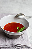 From above served spanish gazpacho tomato cream soup on light grey concrete background with fresh basil herb