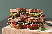 Delicious pastrami sandwich made with wholegrain bread with fresh salad and pickle served on wooden board