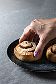 Cropped unrecognizable person holding cinnamon roll bun, Kanelbulle traditional Swedish dessert served in black plate